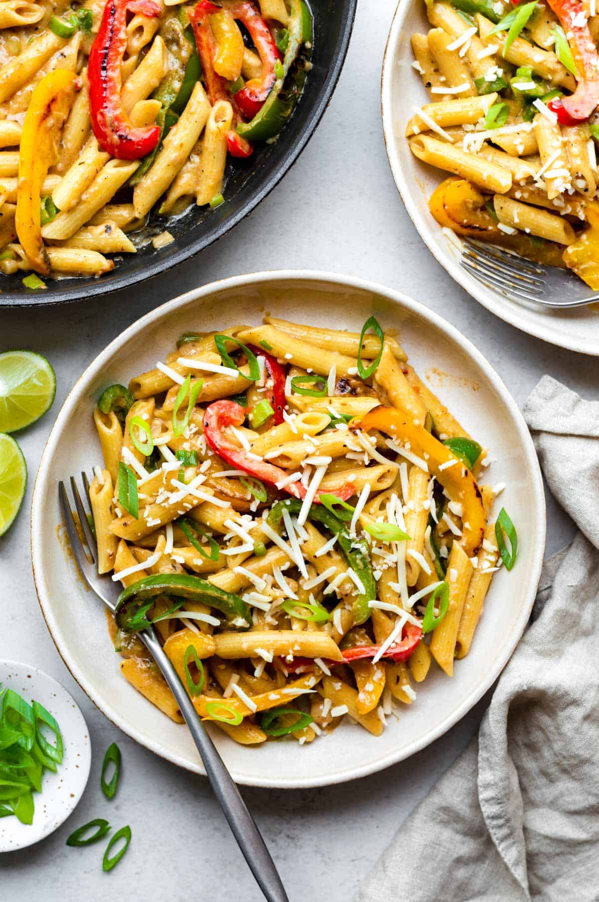 Vegetarian rasta pasta served in a creme bowl and topped with vegan cheese shreds and chopped green onion.