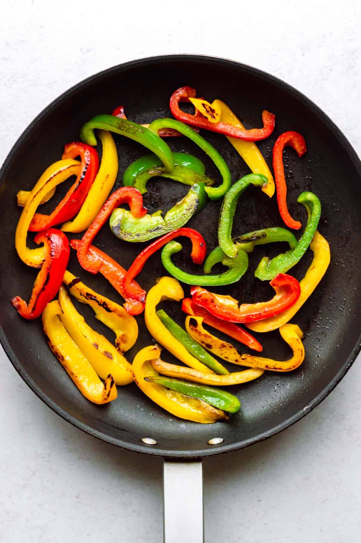 Sauteing strips of green, red, and yellow bell peppers in a skillet.