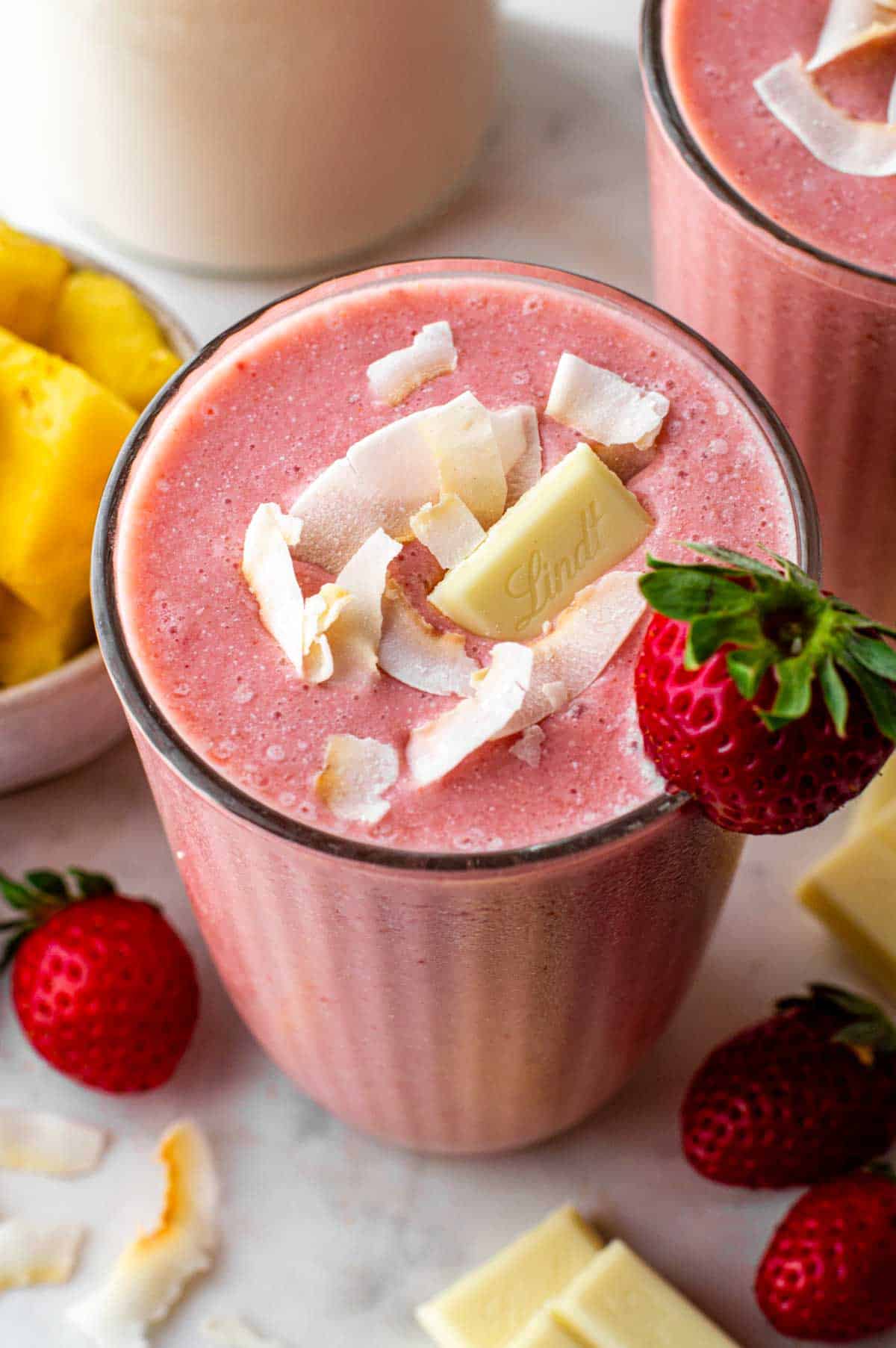 Strawberry smoothie served in a glass jar and topped with coconut, white chocolate and a strawberry.