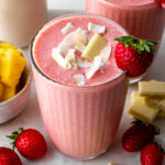 A glass of Bahama mama tropical smoothie topped with coconut flakes and white chocolate.