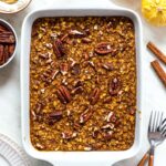A ceramic baking dish filled with baked oatmeal, topped with chopped pecans.
