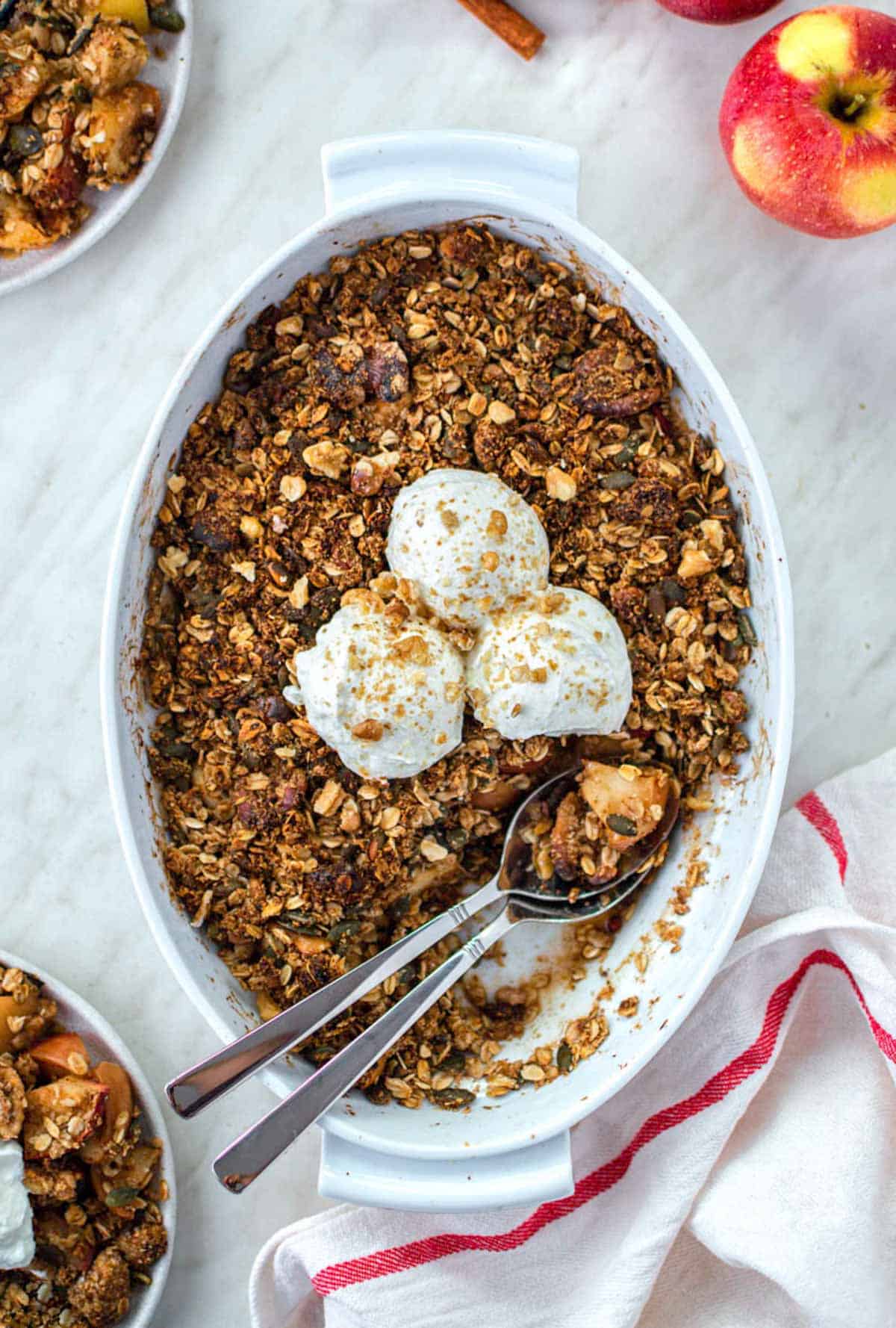 Apple crisp in a baking dish, topped with 3 scoops of yogurt and crushed walnuts.