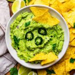 A white bowl filled with guacamole, with tortilla chips surrounding it.