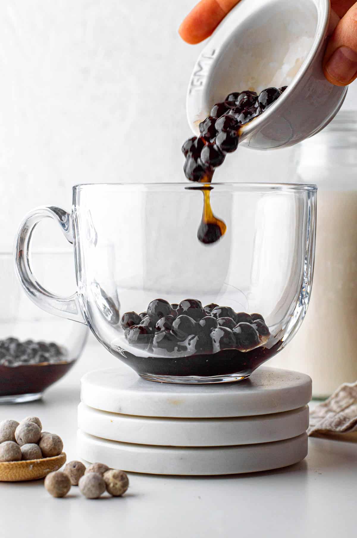 Pouring tapioca pearls from a small white bowl to a large glass.