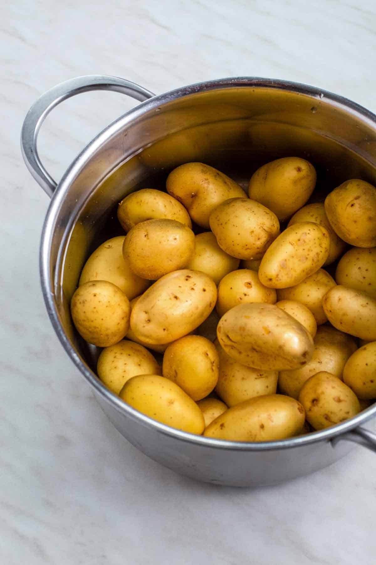 Baby potatoes in a stainless steel pot filled with water.