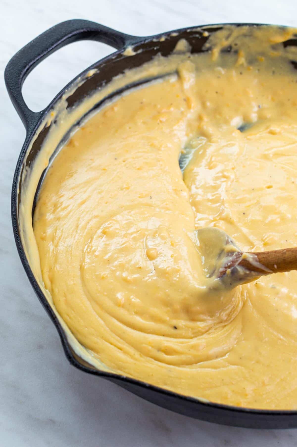 Vegan mac and cheese sauce without cashews in a skillet stirred with a wooden spoon.