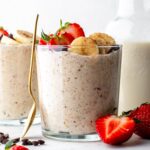 Flaxseed overnight oats in a glass cup topped with banana slices and halved strawberries.