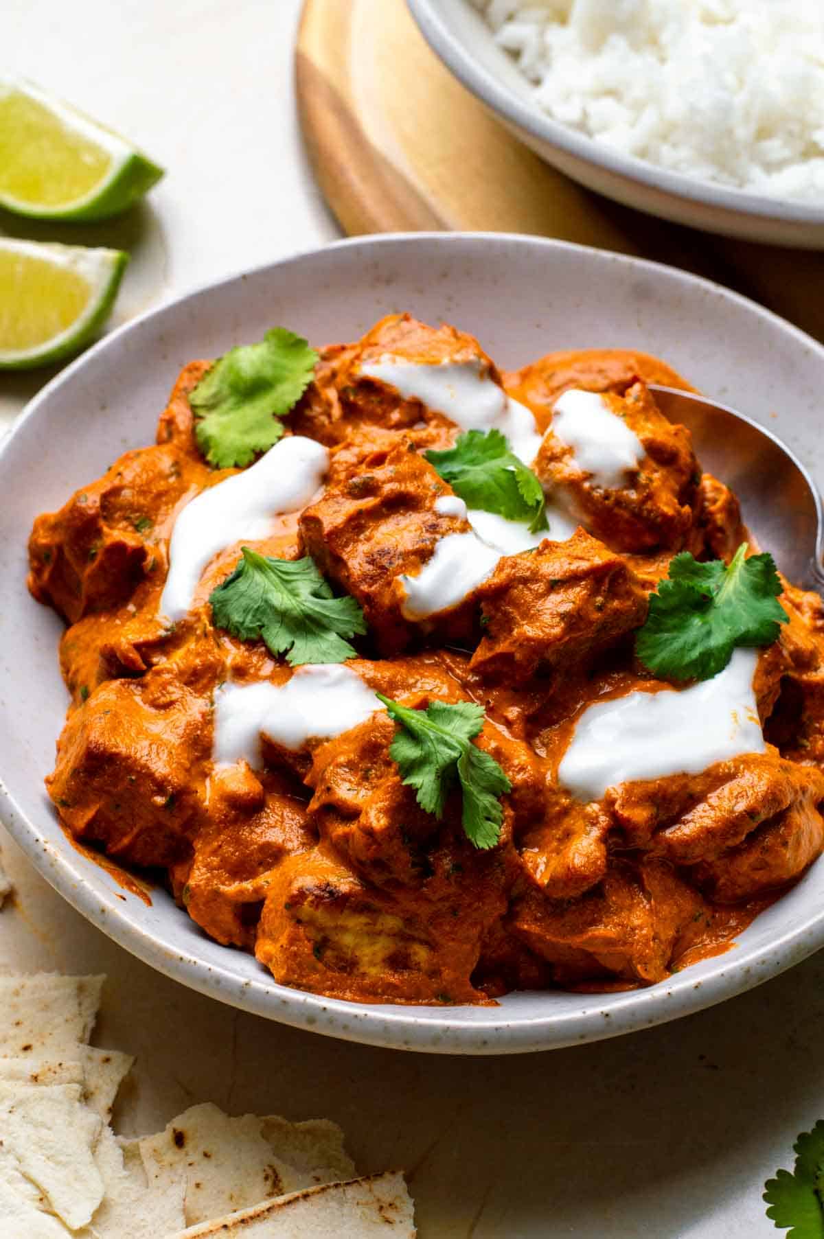 A white bowl filled with tofu curry topped with cilantro leaves and yogurt.