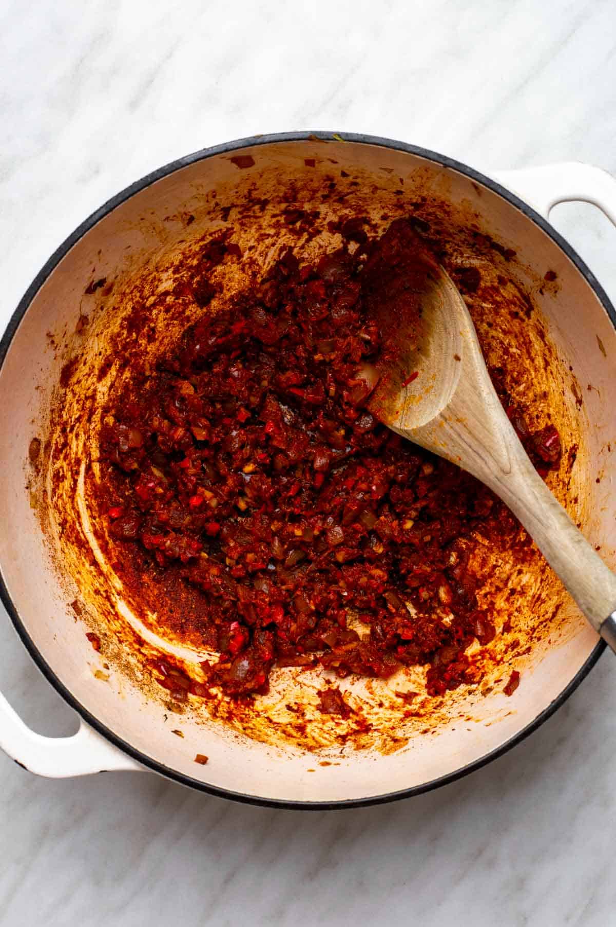 Aromatics and tomato paste in a white Dutch oven.