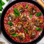 A cast-iron skillet with meatballs in tomato sauce topped with fresh basil and parmesan cheese.