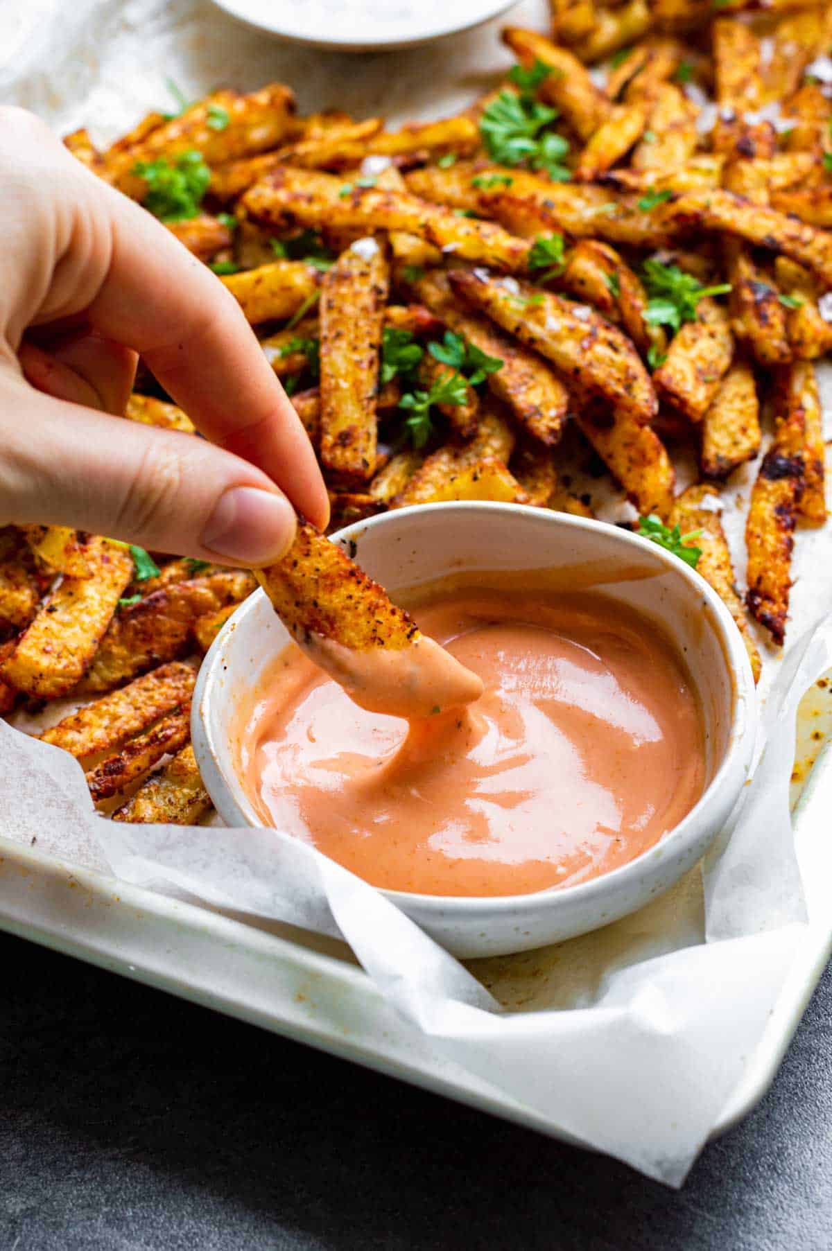 A hand dipping a Cajun fry in a small white bowl filled with pink sauce.