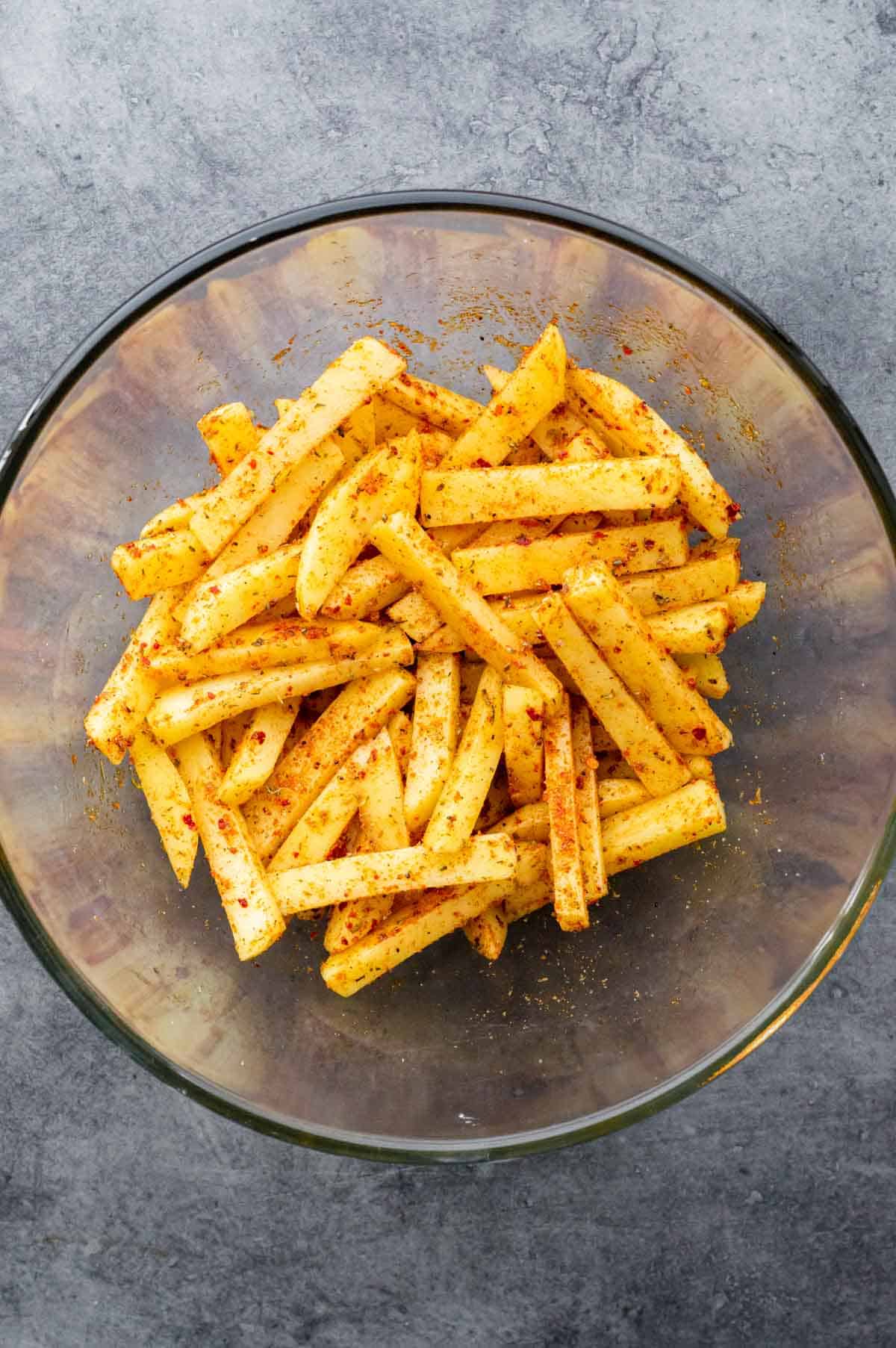 Raw sliced potatoes coated in Cajun seasoning in a large bowl.