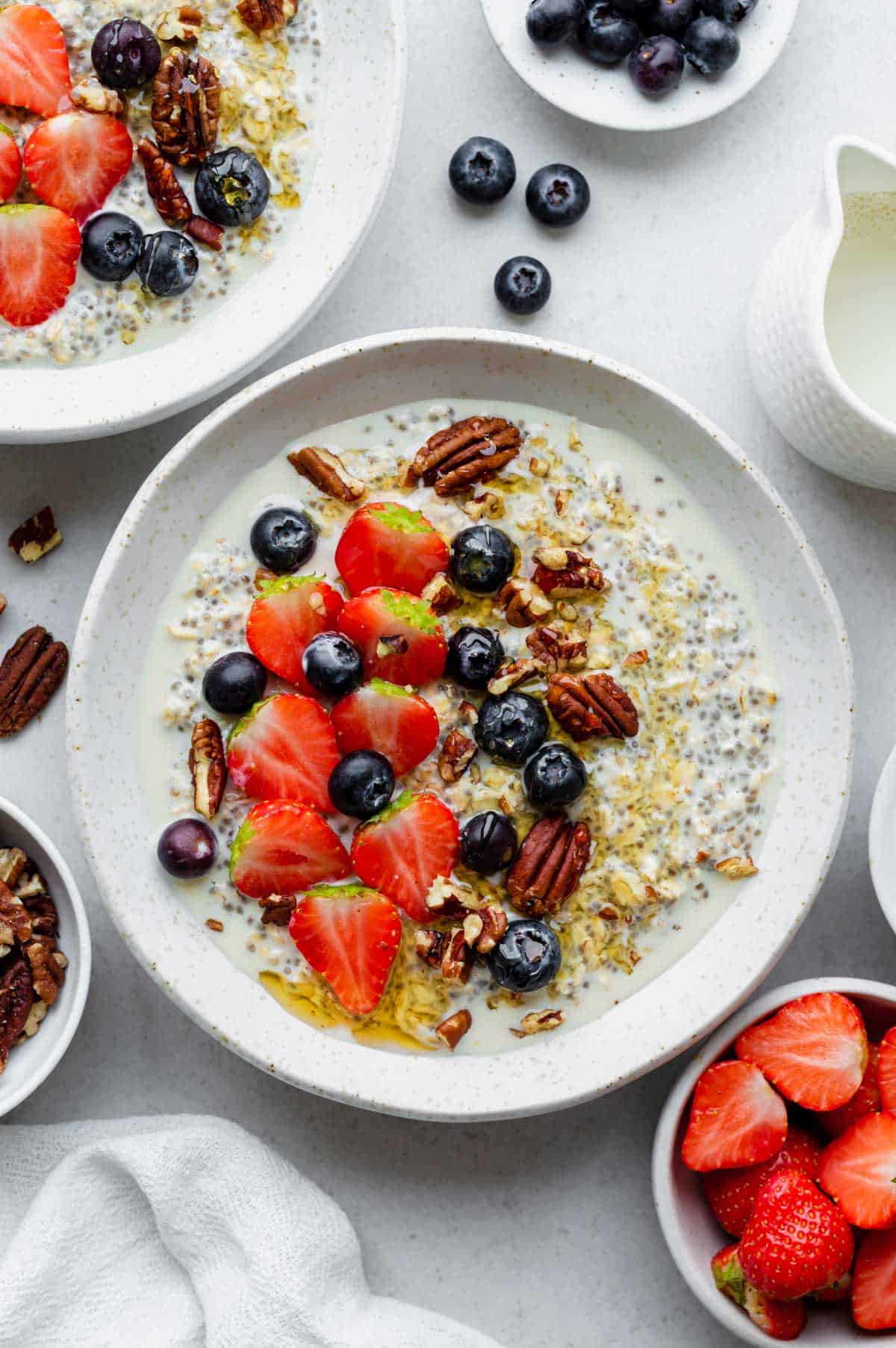 Overnight oats without yogurt served in a white bowl and topped with fresh berries, crushed pecans, and a drizzle of honey.