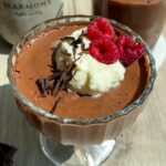 Chocolate aquafaba mousse in a glass cup topped with whipped cream and raspberries.