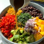 Pouring dressing over the black bean mango salad from a white jug.