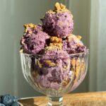 Blueberry pie ice cream in a glass cup, topped with crushed graham crackers.