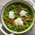 Broccoli pasta in a white Dutch oven, topped with burrata cheese and sliced red chili.