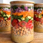 Quinoa chickpea salad jars on a wooden cutting board.