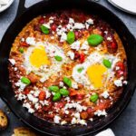 Shakshuka for one in a cast-iron skillet, topped with feta cheese and basil.