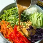 Pouring peanut dressing over spring roll salad.