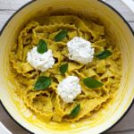 Corn pasta in a white Dutch oven topped with burrata cheese and basil leaves.