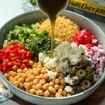 Pouring dressing over a bowl full of chickpea couscous salad.