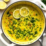 Lemon orzo soup in a white Dutch oven topped with lemon slices and chopped parsley.