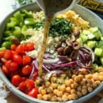Pouring dressing over a big bowl full of Greek pasta salad.