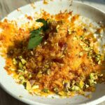 Peach shave ice cream in a white bowl topped with chopped pistachios and fresh mint.
