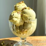 Pistachio ice cream serve in a glass cup and topped with chopped pistachios.