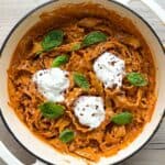 Sun-dried tomato pasta in a white Dutch oven topped with stracciatella cheese.