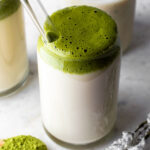 A tall glass filled with milk and topped with dalgona matcha.