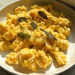 Pumpkin feta pasta on a white plate topped with fried sage leaves.