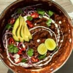 Black bean chili in a white Dutch oven topped with avocado slices, cilantro and cashew cream.