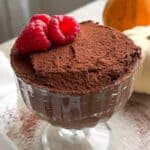 Pumpkin chocolate mousse in a glass cup topped with cocoa powder and raspberries.