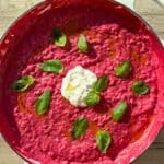 Beet risotto in a white Dutch oven topped with burrata cheese and fresh basil.