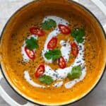 Red lentil dahl in a white dutch oven toped with yogurt, cilantro, red chili and black sesame seeds.