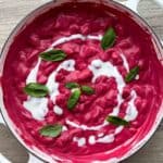Butter beans in a pink beet sauce in a white Dutch oven.