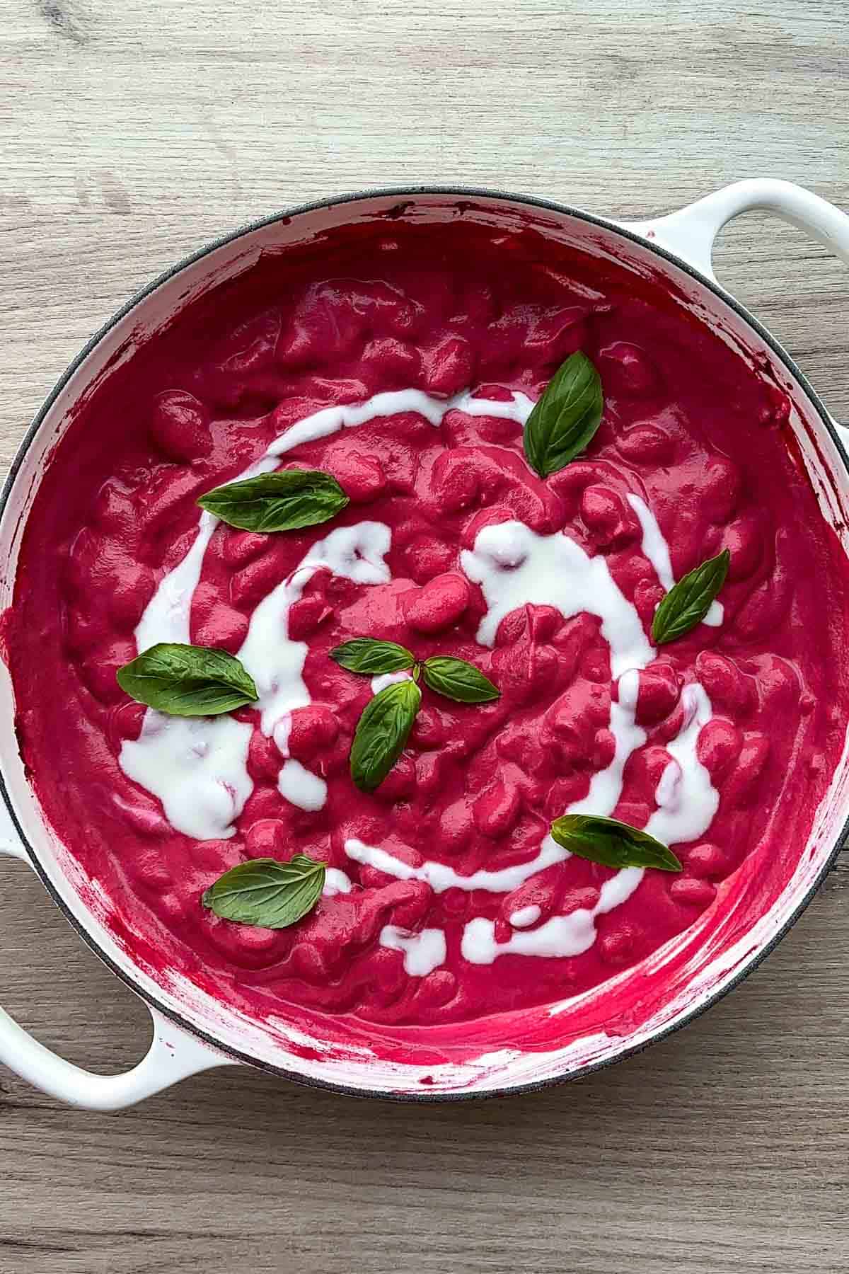 Butter beans in a pink beet sauce in a white Dutch oven.