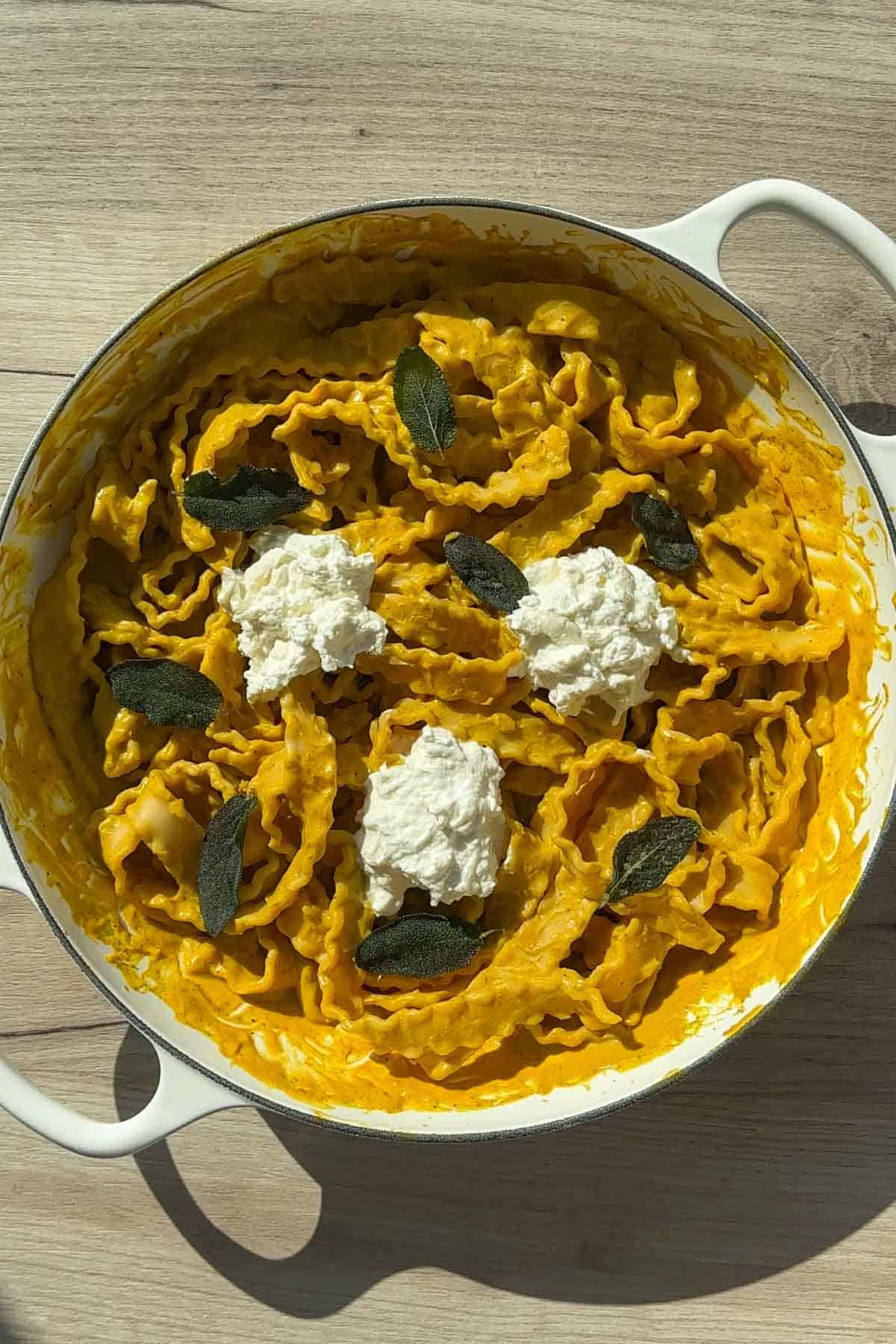 Pumpkin sage pasta in a white Dutch oven topped with burrata cheese.
