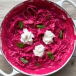 Beet pasta in a white Dutch oven topped with stracciatella cheese an fresh basil leaves.