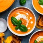 Pumpkin tomato soup served in a bowl and topped with cream, olive oil and fresh basil.