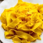 A white plate with saffron pasta topped with saffron petals.