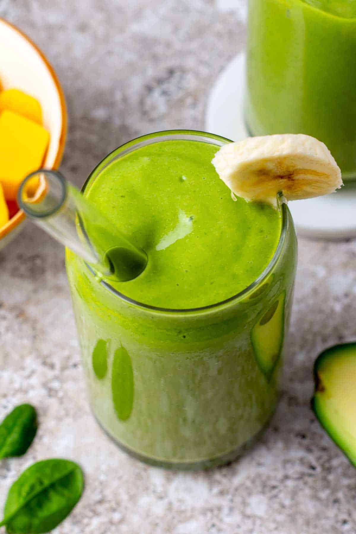 An avocado banana smoothie on a table with a glass straw. 
