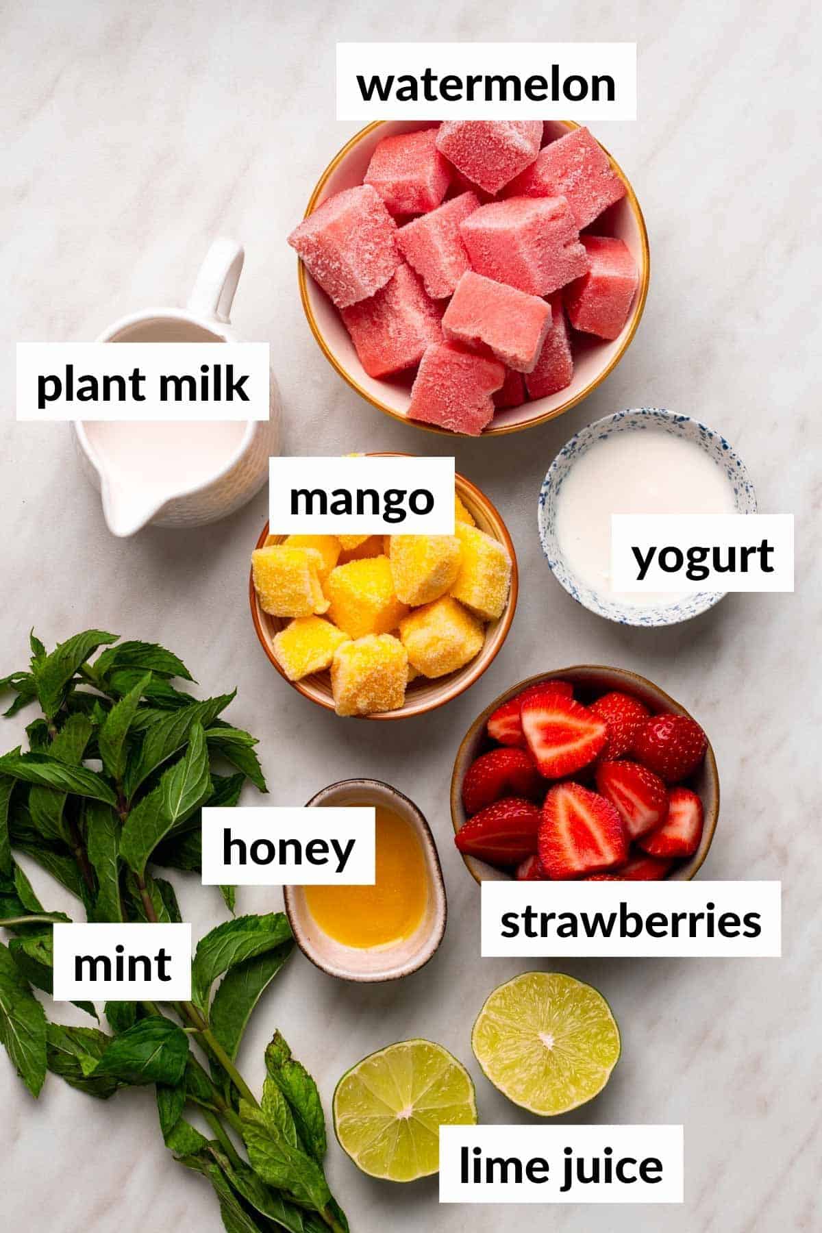 Ingredients to make a mango smoothie on the table with text labels for each ingredient.
