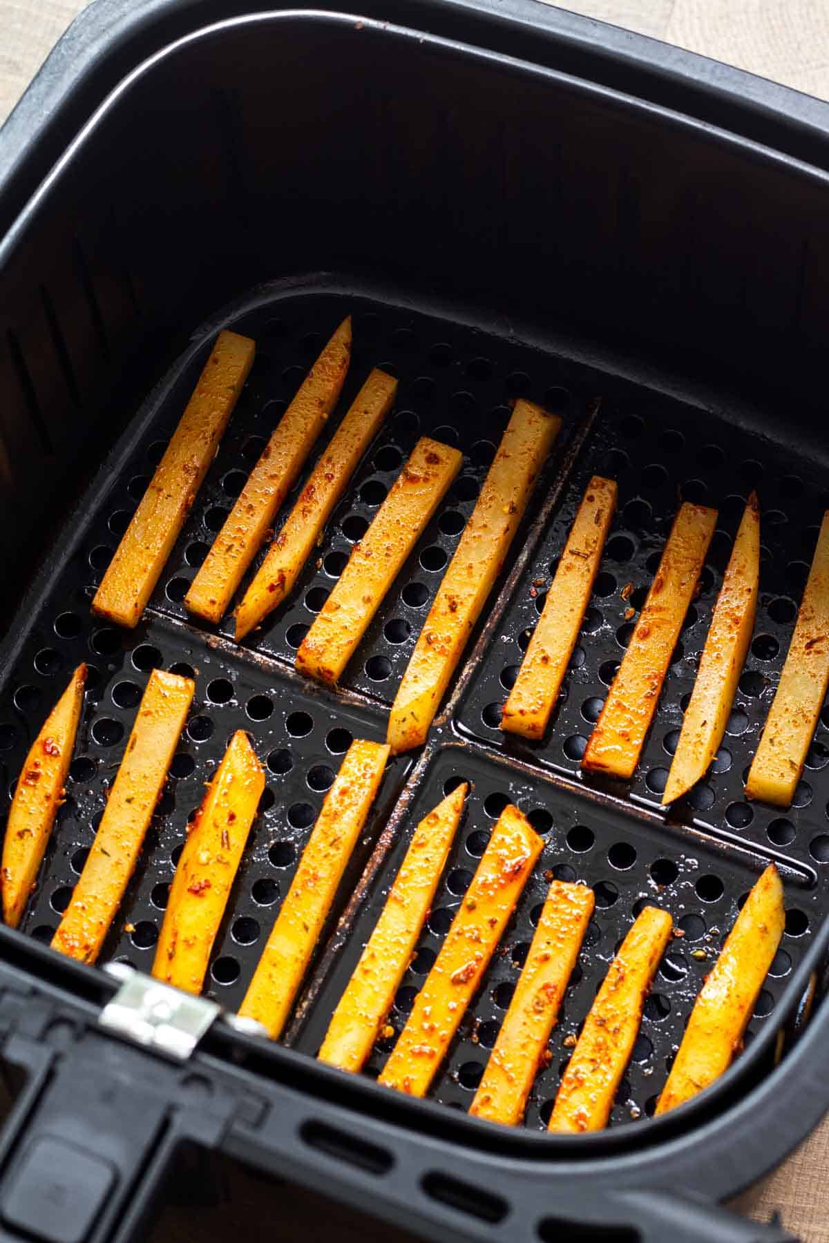 Cajun fries arranged in an air fryer basket ready to be cooked.