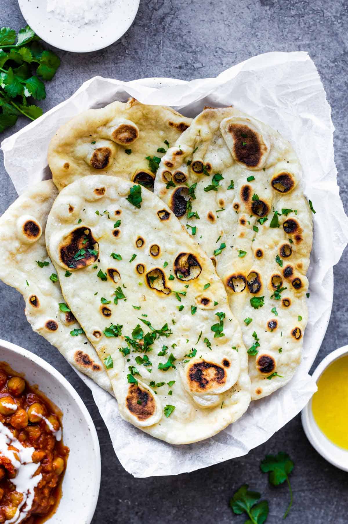 A few pieces of naan bread served in a white bowl layered with parchment paper, topped with chopped cilantro.