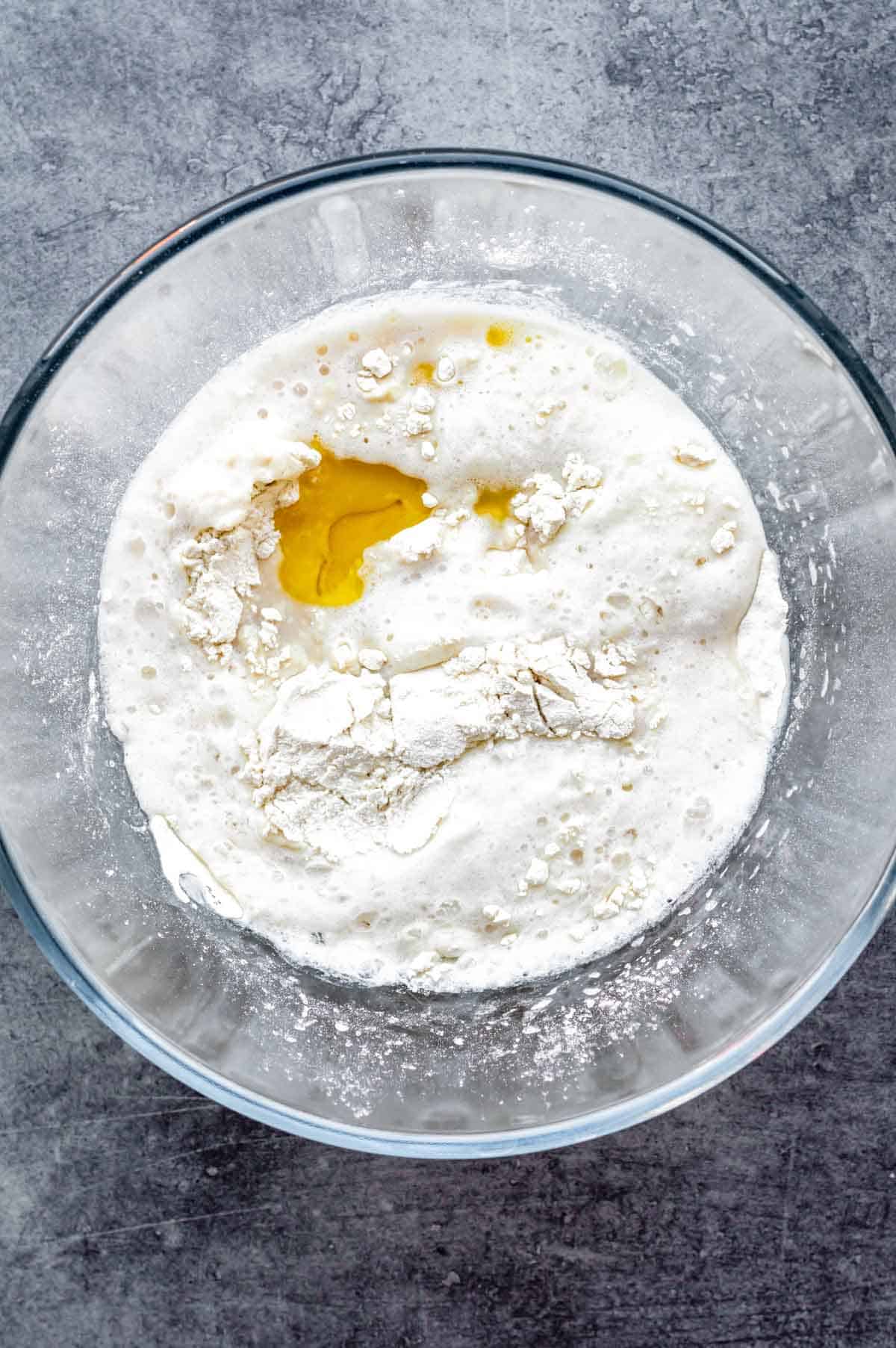 Flour, yeast, olive oil and almond milk in a glass bowl, ready to be stirred for naan dough.