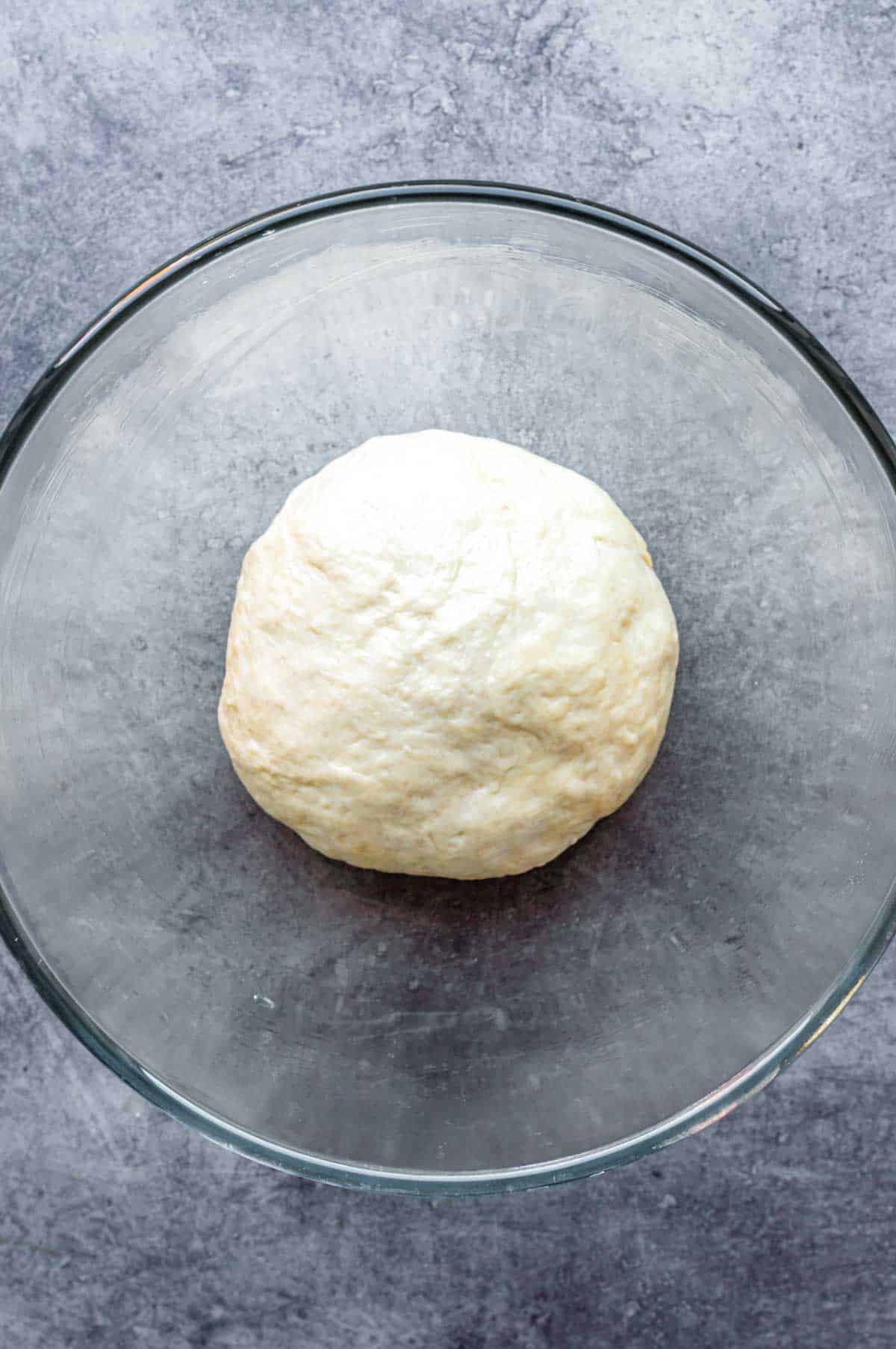 Kneaded naan dough in a glass bowl.