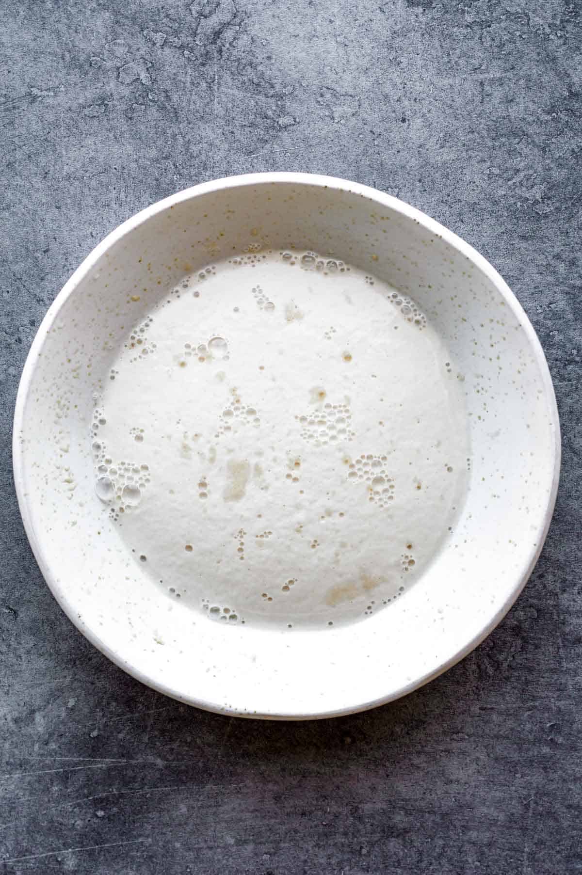 Blooming yeast for naan dough in a white bowl.